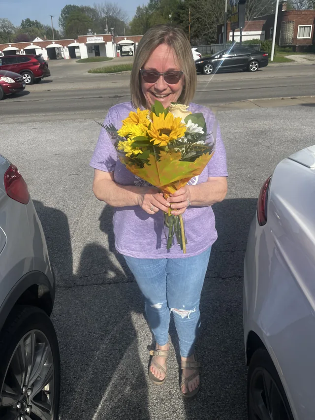 A person smiling while holding yellow flowers