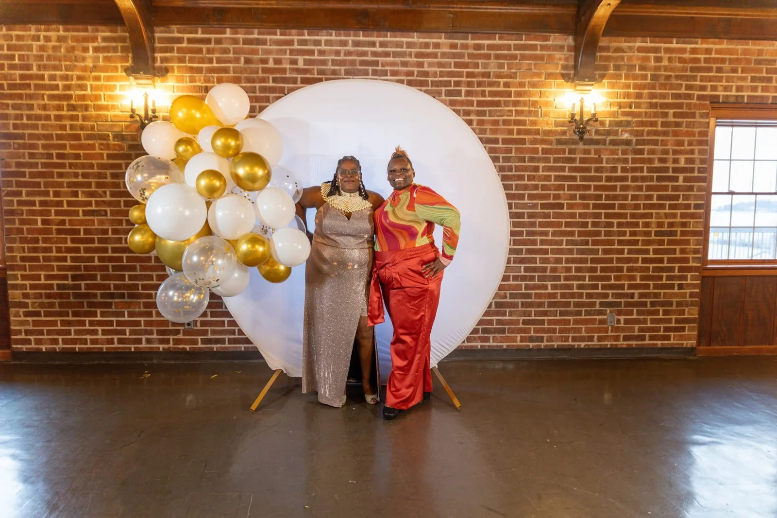 Two people beside a white and gold balloon display