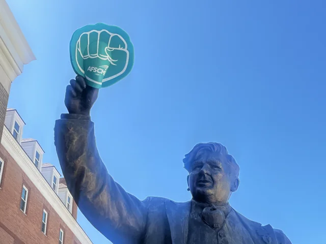 An AFSCME raised-fist symbol held near an outdoor statue