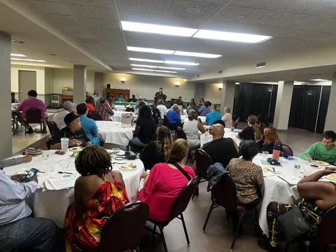 A room of participants seated around tables at a gathering. Alternate view 2.