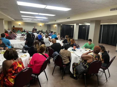 A room of participants seated around tables at a gathering. Alternate view 3.