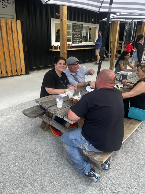 Participants sharing food and conversation at outdoor picnic tables.