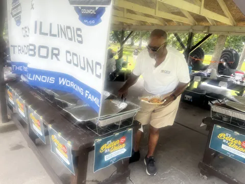Food is served under a picnic shelter beside an Illinois labor council banner.