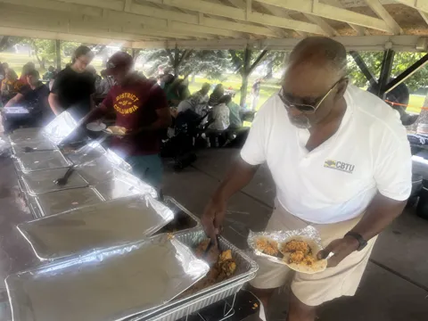 Food is served under a picnic shelter beside an Illinois labor council banner. Alternate view 2.