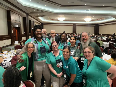 A group wearing green gathers for a photograph around a table in a meeting hall.
