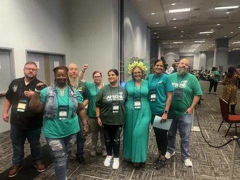 A group wearing green AFSCME clothing poses together in a meeting hall.