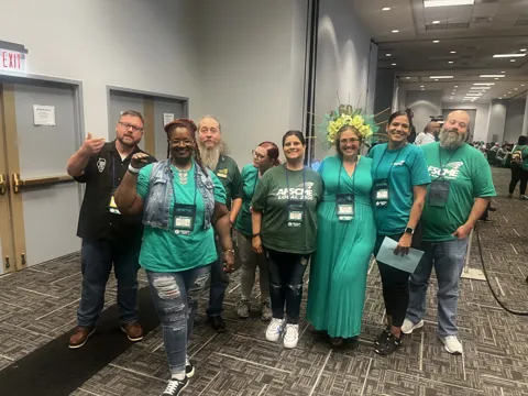 A group wearing green AFSCME clothing poses together in a meeting hall. Alternate view 3.