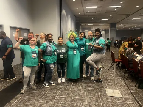 A group wearing green AFSCME clothing poses together in a meeting hall. Alternate view 6.