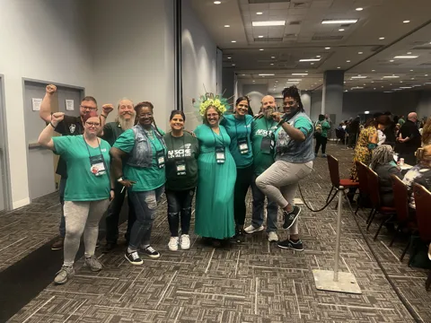 A group wearing green AFSCME clothing poses together in a meeting hall. Alternate view 9.