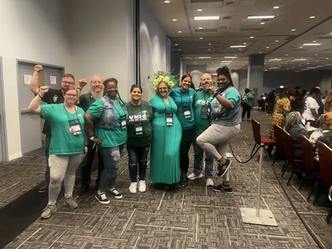 A group wearing green AFSCME clothing poses together in a meeting hall. Alternate view 10.