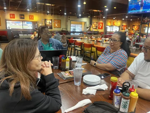 Participants share a meal and conversation at a restaurant table.