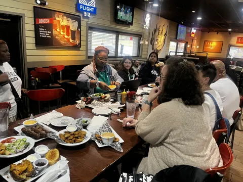 Participants share a meal and conversation at a restaurant table. Alternate view 2.