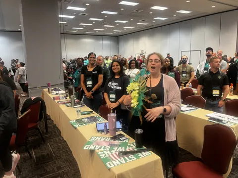Participants gather around a decorated table in a meeting hall. Alternate view 2.