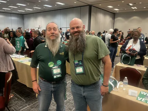 Two participants with long beards pose together in a meeting hall.
