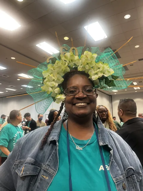 A smiling participant wears a large green and yellow decorated hat.