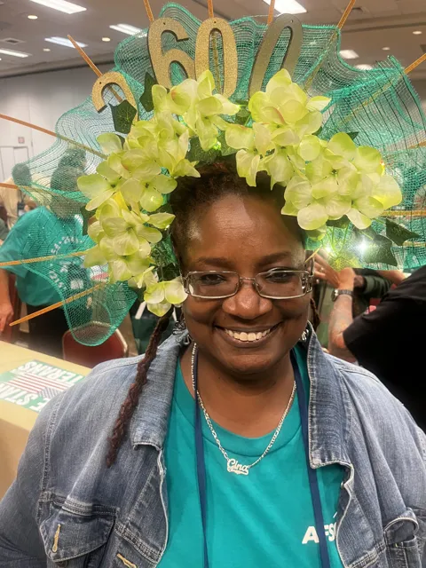 A smiling participant wears a large green and yellow decorated hat. Alternate view 4.