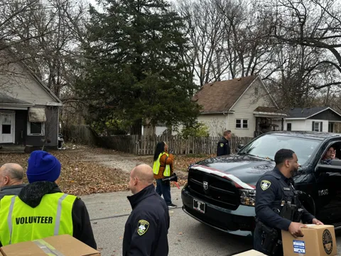 Participants speak outdoors beside a vehicle; some wear volunteer vests and others wear uniforms. Alternate view 2.