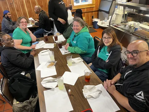 Participants share a meal at a long restaurant table. Alternate view 2.