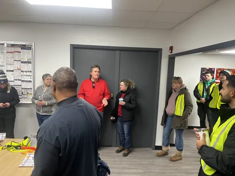Participants gather in an office meeting space, some wearing high-visibility vests. Alternate view 2.