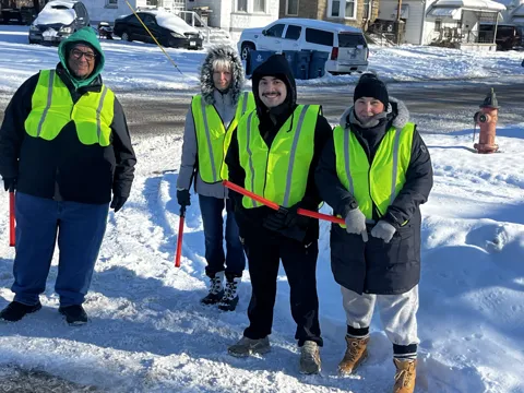Participants in high-visibility vests pose together outdoors in the snow. Alternate view 9.