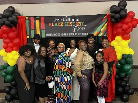 A group poses beneath a Black History Month banner framed by red, yellow, green and black balloons. Alternate view 2.