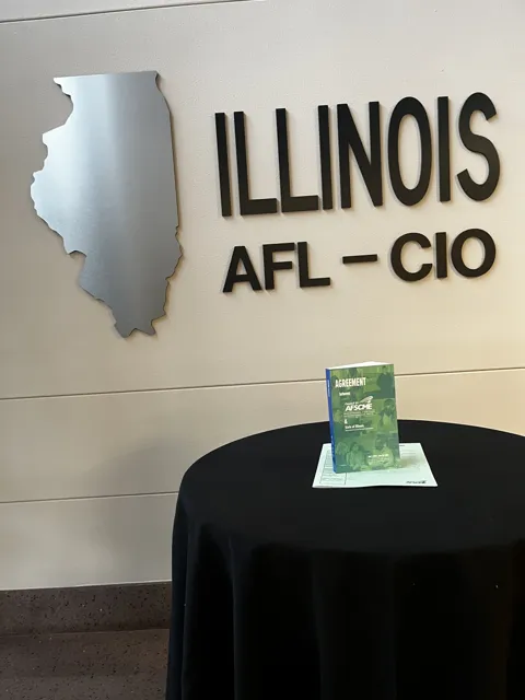 An agreement booklet displayed on a table beneath an Illinois AFL–CIO sign.