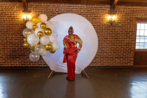A guest poses beside a white and gold balloon display.