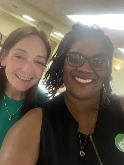 Two people smile for a selfie indoors.