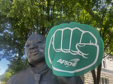 An AFSCME raised-fist symbol beside an outdoor statue.