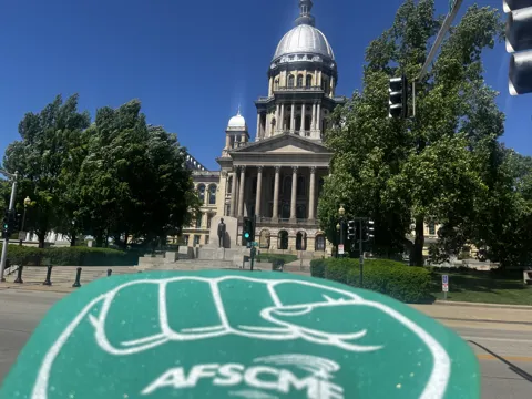 An AFSCME raised-fist symbol in front of the Illinois State Capitol.