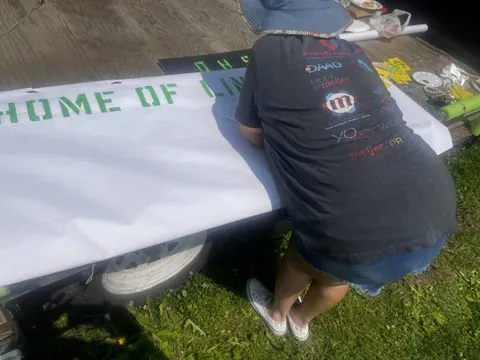 A participant works on a large banner outdoors. Alternate view 4.