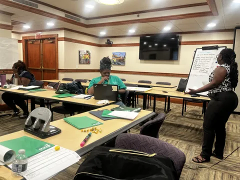 Participants seated around tables during a group discussion and presentation. Alternate view 2.