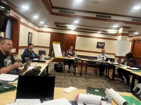 Participants seated around tables during a group discussion and presentation. Alternate view 3.