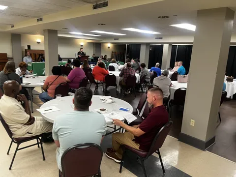 A room of participants seated around tables at a gathering.